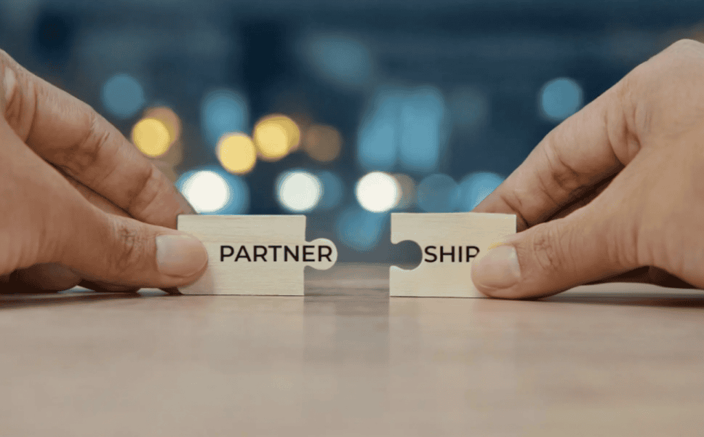 Man connecting two puzzle pieces that spell partnership